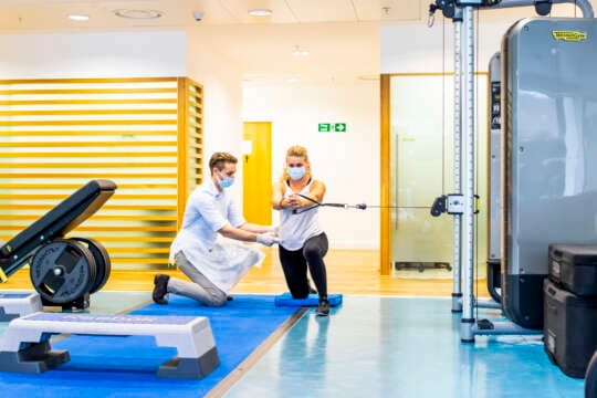 patient with pulley machine and clinician supporting